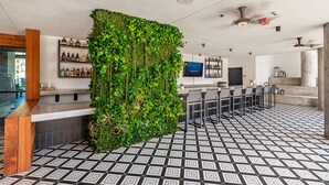 A modern bar area with a green vertical garden, a tiled floor, and a bar counter with shelves of bottles.