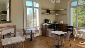 Comedor con piso de madera, una isla central con cafetera y ventanas amplias que ofrecen vista a árboles.