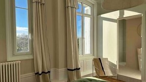 Un dormitorio con un ventanal grande, un radiador, una cama y una silla.