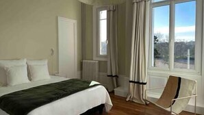 Un dormitorio con cama, una silla, un radiador y una ventana con cortinas.