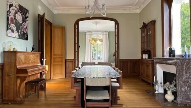 Een eetzaal met een marmeren tafel, houten stoelen, een kroonluchter en uitzicht door een open deur.