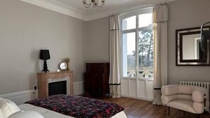 Een slaapkamer met een bed, een kaptafel, een stoel, een open haard en een raam met gordijnen.