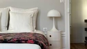 Een slaapkamer met een bed, kussens, een nachtkastje en een lamp.