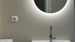 Un baño con un espejo redondo, un lavamanos blanco y un interruptor de luz visible en la pared.