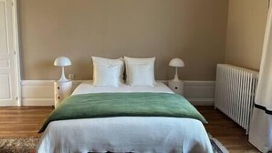 Un dormitorio con una cama, dos lámparas de noche, un radiador y una manta verde.