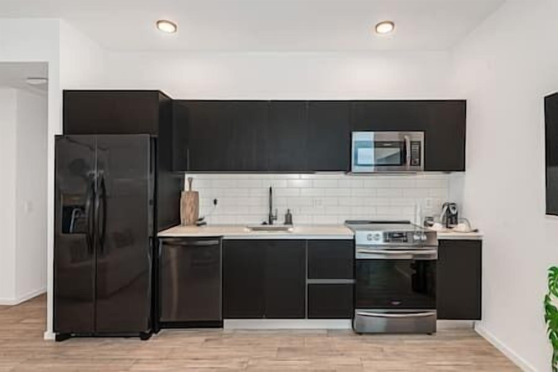 A modern kitchen with dark cabinets, a stainless steel refrigerator, a microwave, and an oven.