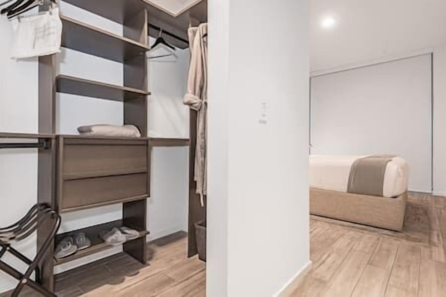 Een moderne slaapkamer met een houten vloer, een beige bank en een inbouwkast met planken en hangruimte.