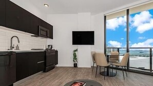 A modern kitchen with dark cabinetry, a flat-screen TV mounted on the wall, and a dining area with a round table and chairs.