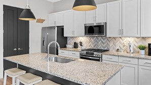 A modern kitchen with white cabinets, granite countertops, stainless steel appliances, and pendant lighting.