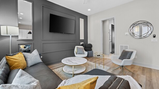 A modern living room with a grey sofa, a round coffee table, and a flat-screen TV mounted on the wall.