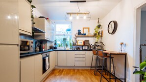 Cocina compacta con armarios blancos, encimera de madera, horno integrado, microondas, lámpara colgante y ventana que proporciona luz natural.