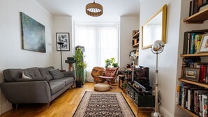 Una sala de estar con sofá, sillón, lámpara de pie, estantería y un espejo grande.