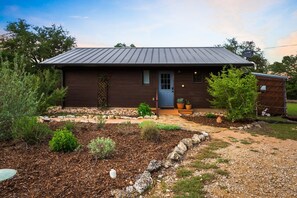 A single-story wooden house with a metal roof, a front door, and a small porch area.