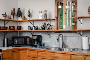 Una cocina con armarios de madera, microondas, cafetera y estantes con objetos decorativos.