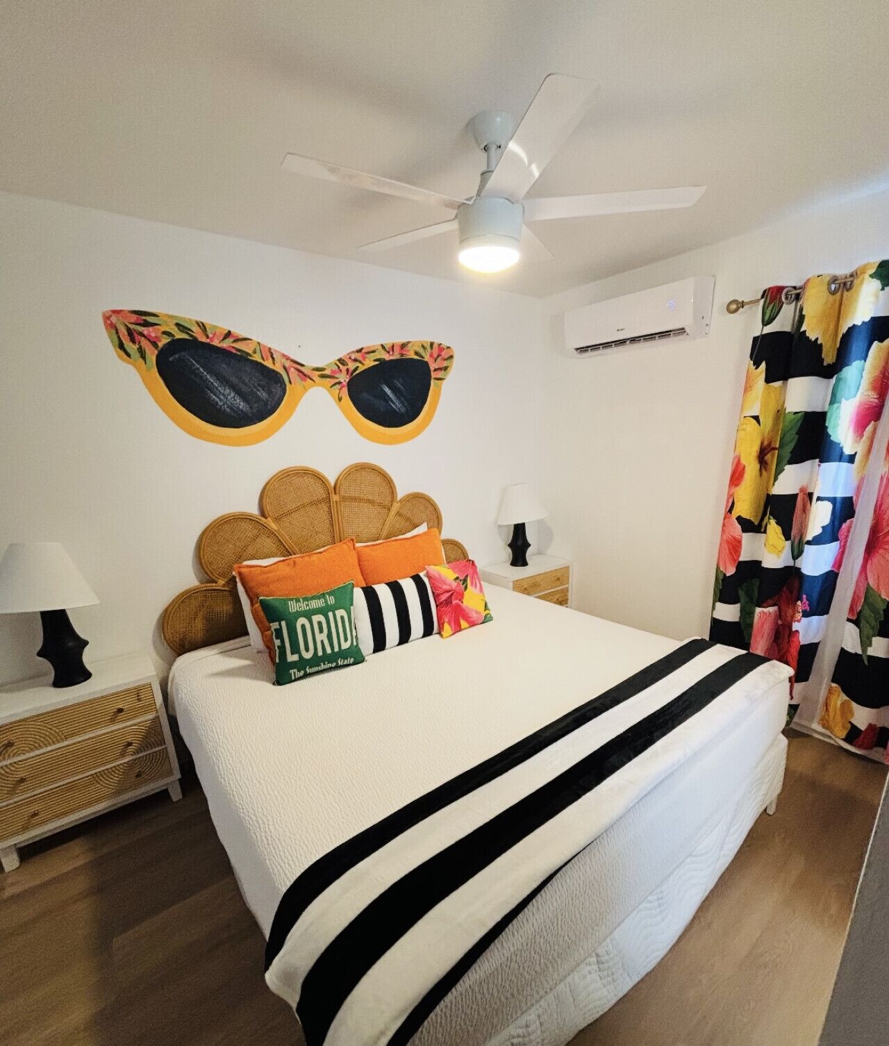 A bedroom with a bed, a ceiling fan, a wall-mounted air conditioner, and a floral curtain.
