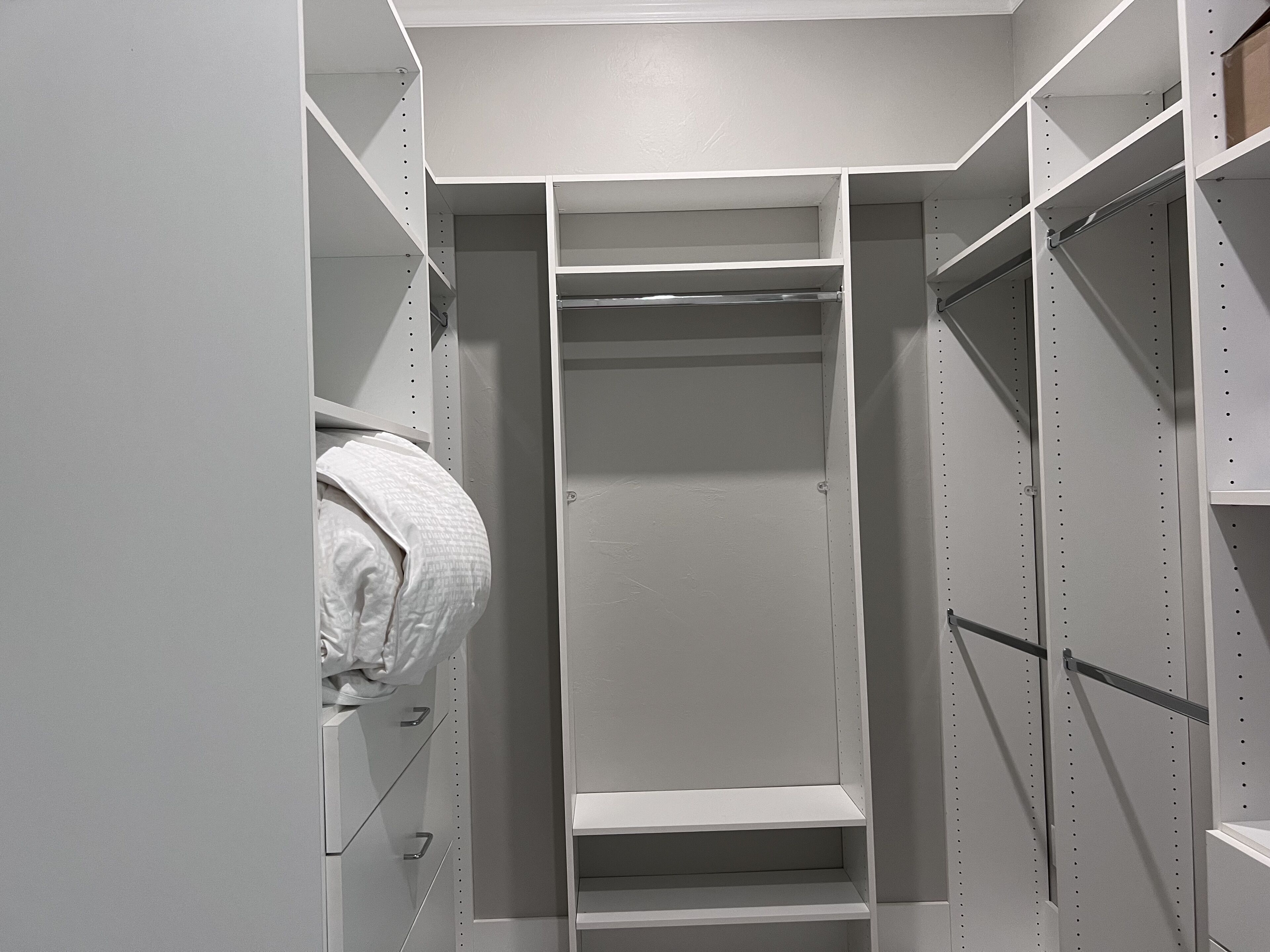 A walk-in closet with multiple shelves and hanging space, featuring a metal rod for hanging items.