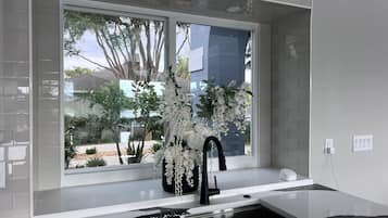 Eine moderne Küche mit großem Fenster, weißen Arbeitsflächen und einem schwarzen Wasserhahn.