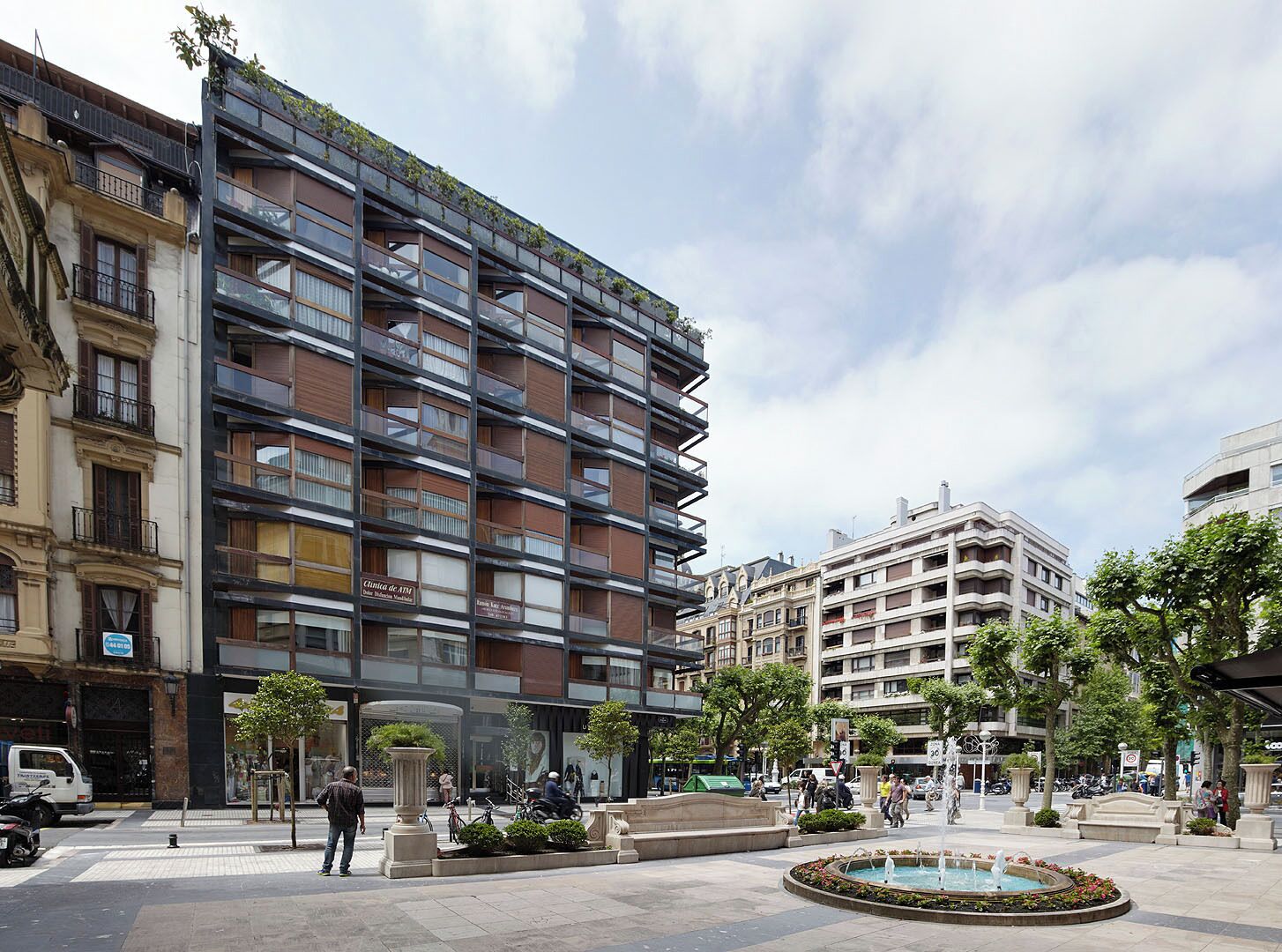 A modern multi-story building with balconies and a courtyard with a fountain.