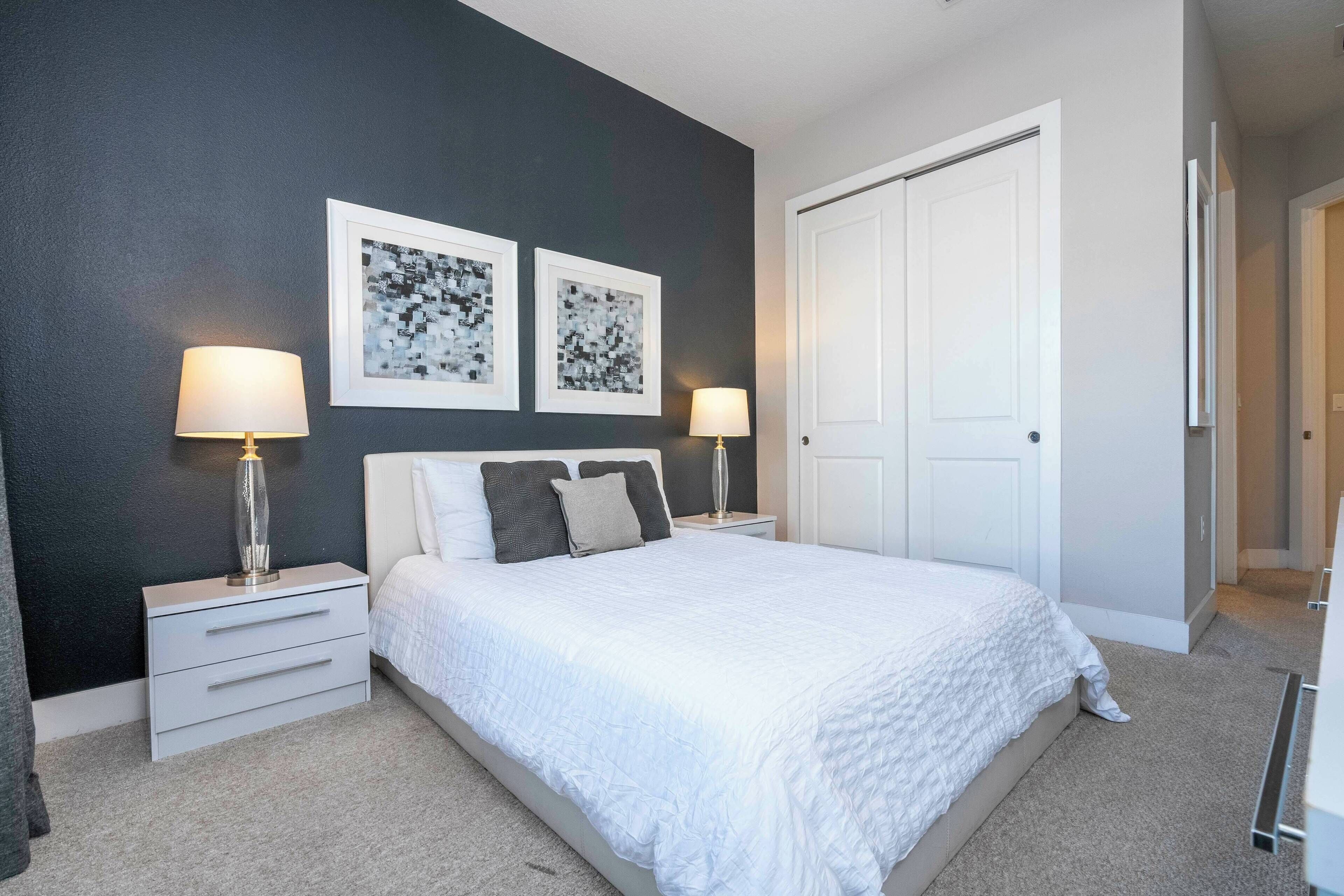 A bedroom with a bed, two bedside tables, a nightstand, a door, and two wall-mounted lamps.