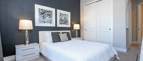 A bedroom with a bed, two bedside tables, a nightstand, a door, and two wall-mounted lamps.