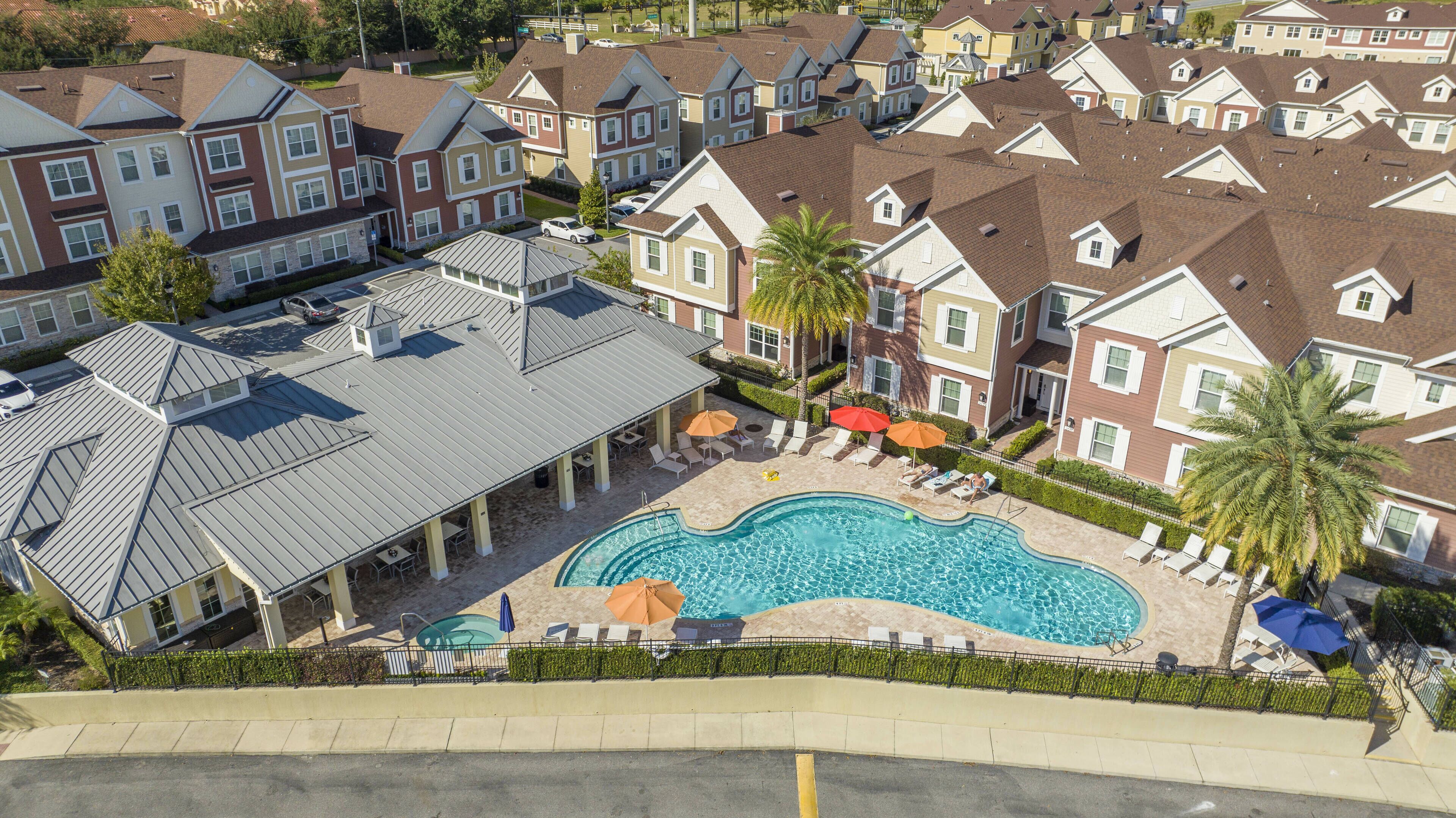 Ein Wohngebiet mit Swimmingpool, umgeben von Liegestühlen und Sonnenschirmen, sowie einer überdachten Terrasse mit Sitzgelegenheiten.