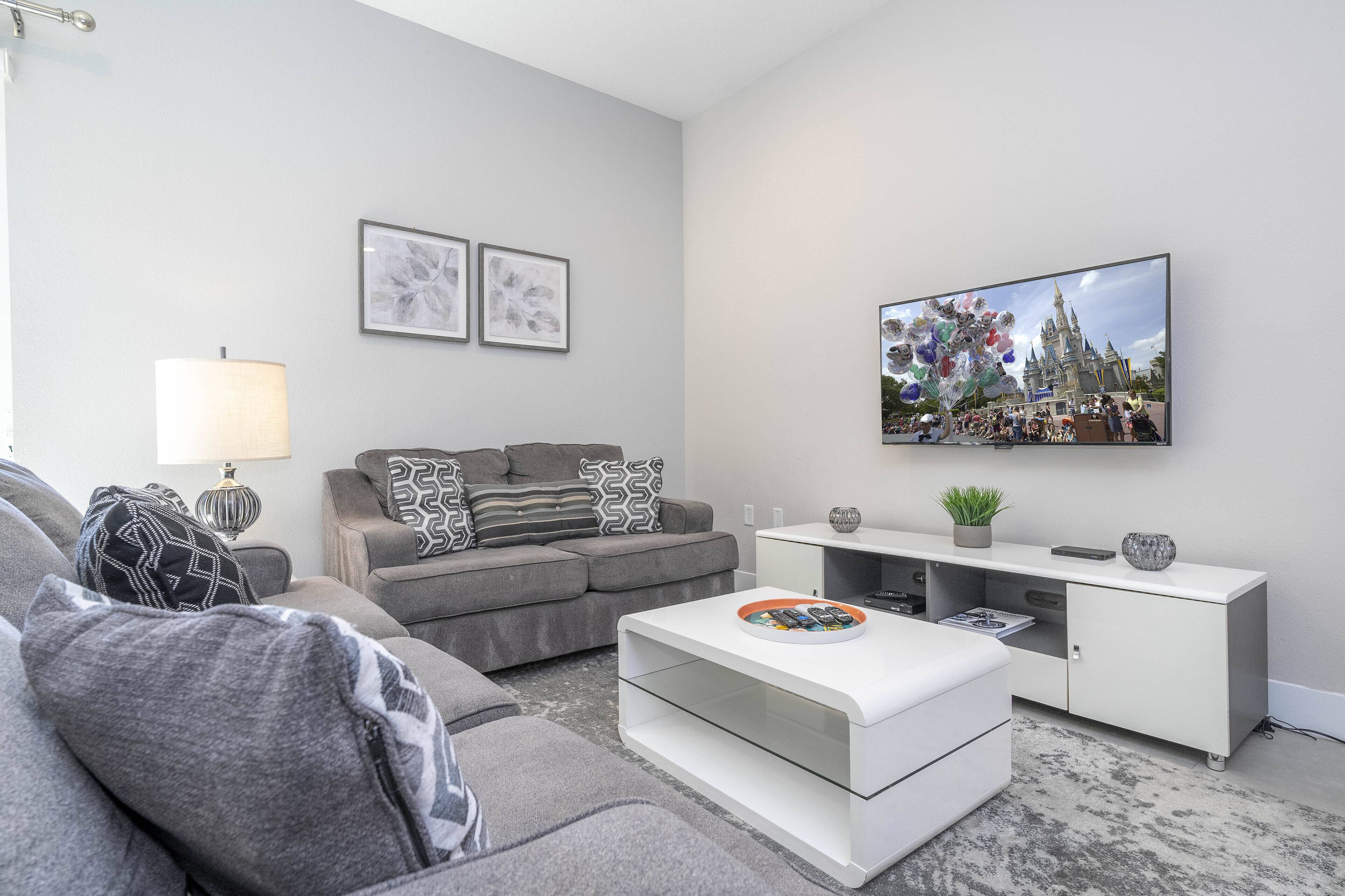 A modern living room with a grey sofa, a white coffee table, and a flat-screen TV mounted on the wall.