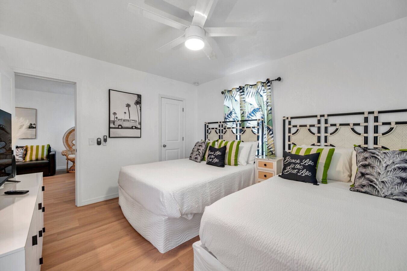 A bedroom with two single beds, a ceiling fan, a door, a framed picture, and a window with curtains.