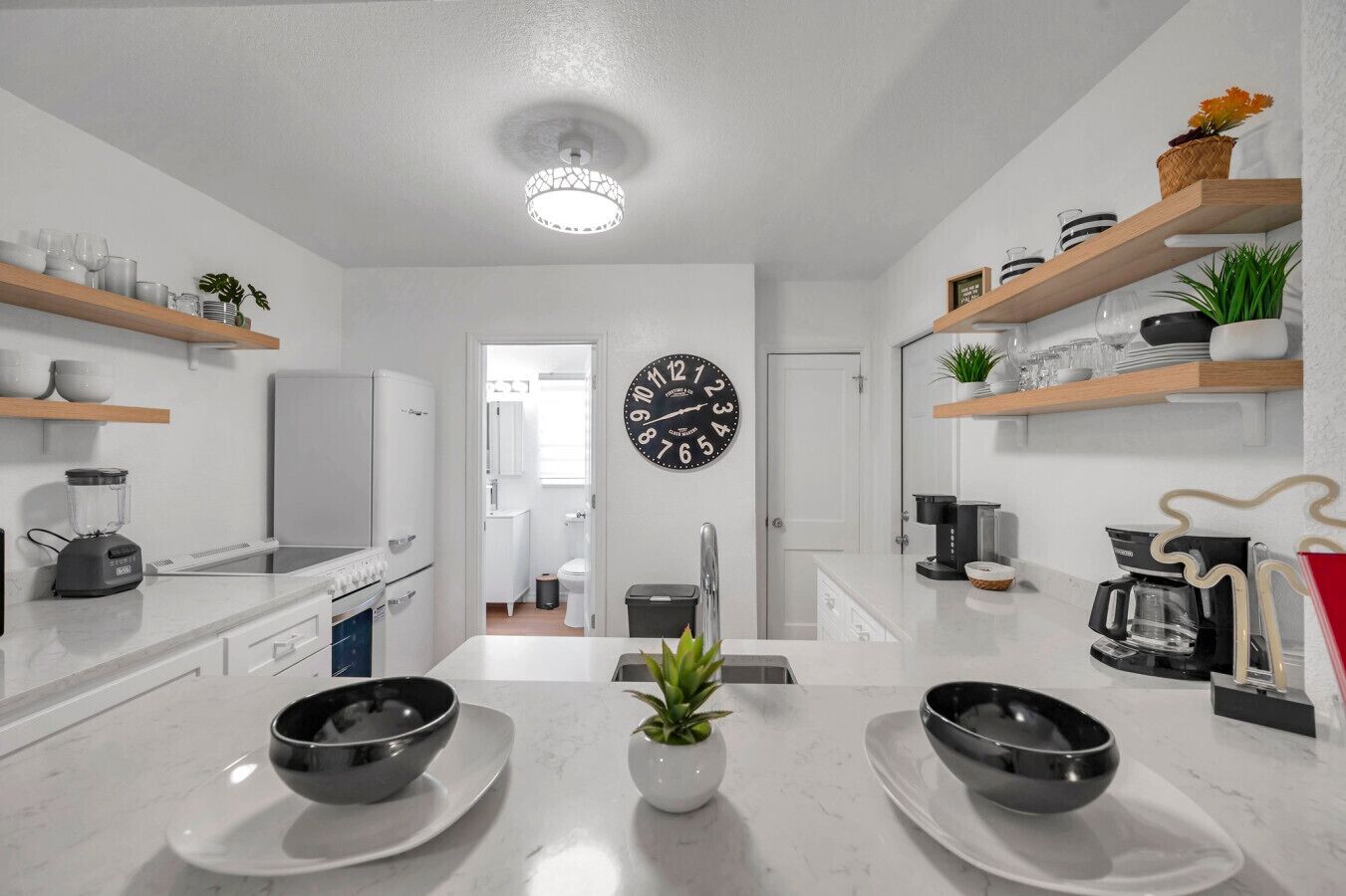 Een moderne keuken met witte aanrechtbladen, een centraal eiland en een klok aan de muur.