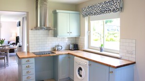 A kitchen with a washing machine, a window with a view, and a dining area in the background. - 4 Bedroom Holiday Home With Wheelchair Accessible Bathroom 2km From Kenmare (Kenmare)