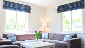A living room with a sofa, a coffee table, and a lamp. There are two windows with curtains. - 4 Bedroom Holiday Home With Wheelchair Accessible Bathroom 2km From Kenmare (Kenmare)
