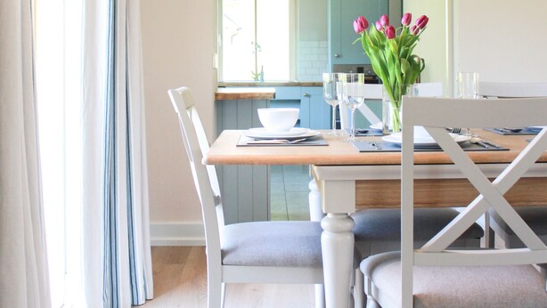 A dining area with a wooden table, white chairs, and a vase of tulips. - 4 Bedroom Holiday Home With Wheelchair Accessible Bathroom 2km From Kenmare (Kenmare)