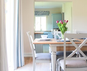A dining area with a wooden table, white chairs, and a vase of tulips. - 4 Bedroom Holiday Home With Wheelchair Accessible Bathroom 2km From Kenmare (Kenmare)