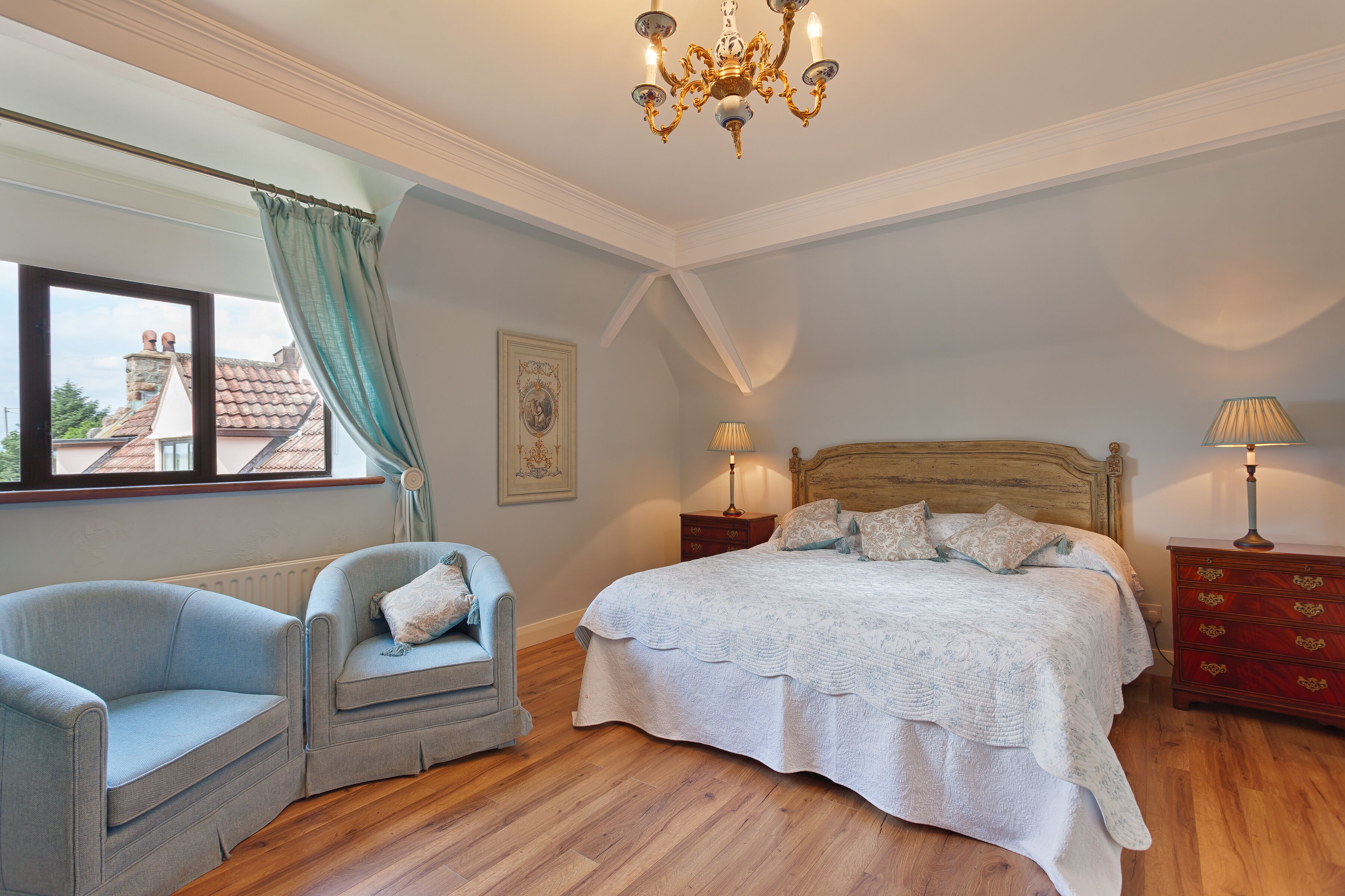 A bedroom with a large bed, a chair, a dresser, and a window with curtains.