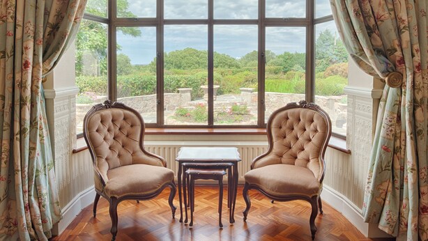A room with two upholstered chairs and a small table, a large window with a view of greenery, and floral curtains. - 8 Bedroom Luxury Country Mansion in Galway (Costelloe)