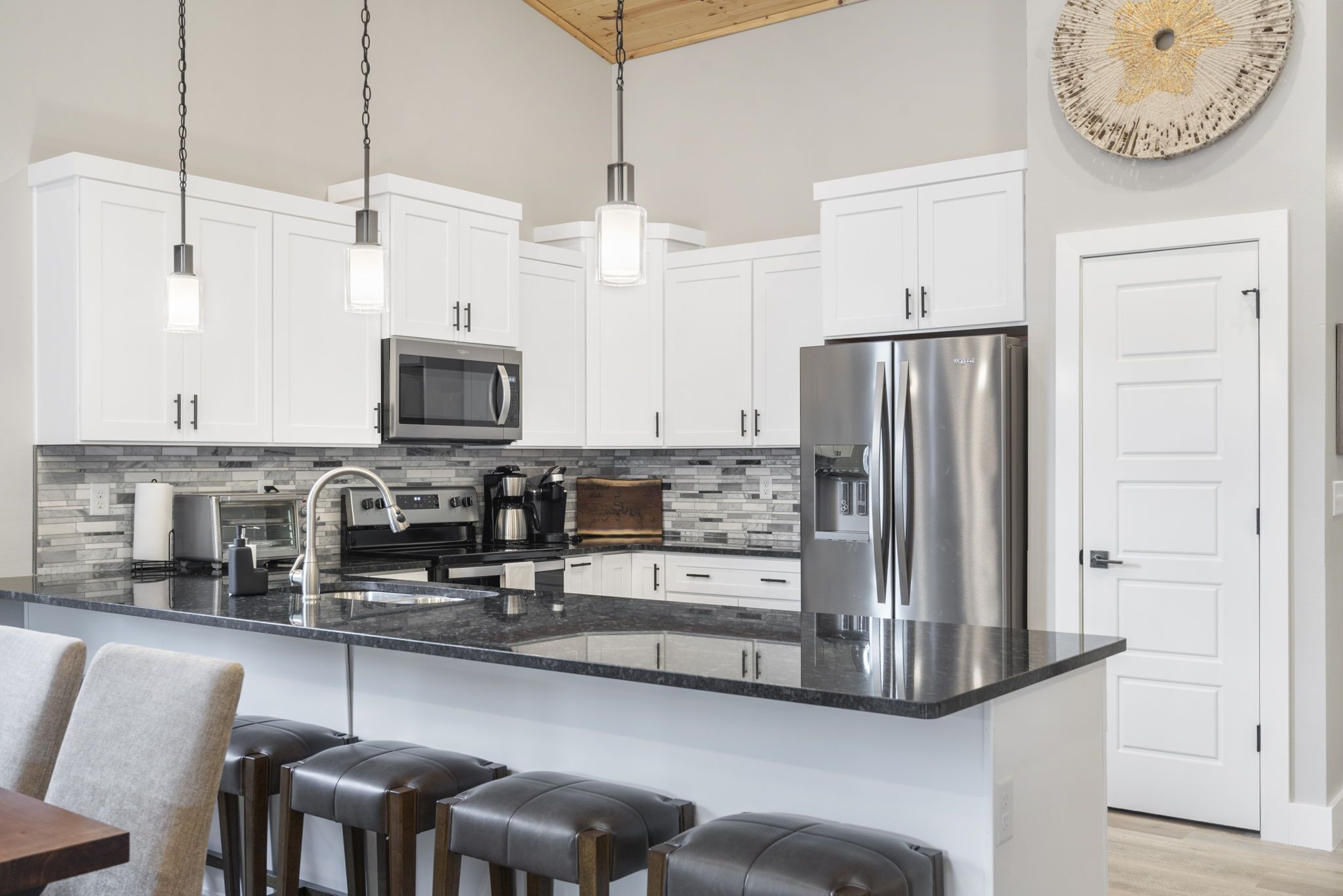 A modern kitchen with white cabinets, stainless steel appliances, a large island with bar stools, and pendant lighting.
