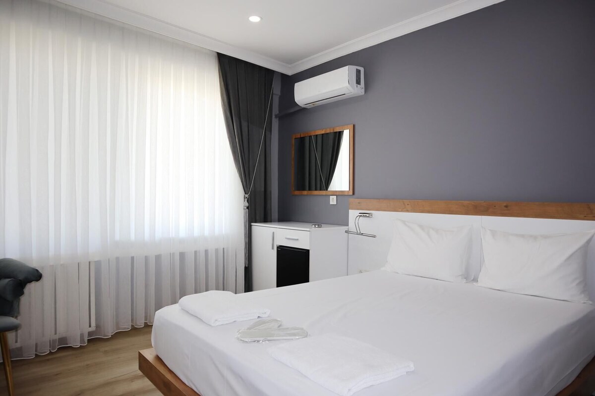 Een hotelkamer met een bed, een bureau, een airconditioning en een raam met gordijnen.