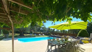 Un patio trasero con piscina, pérgola y zona de comedor con mobiliario exterior.
