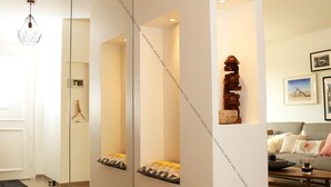 Una sala de estar moderna con un espejo grande, una lámpara colgante geométrica y una escultura de madera en una estantería.
