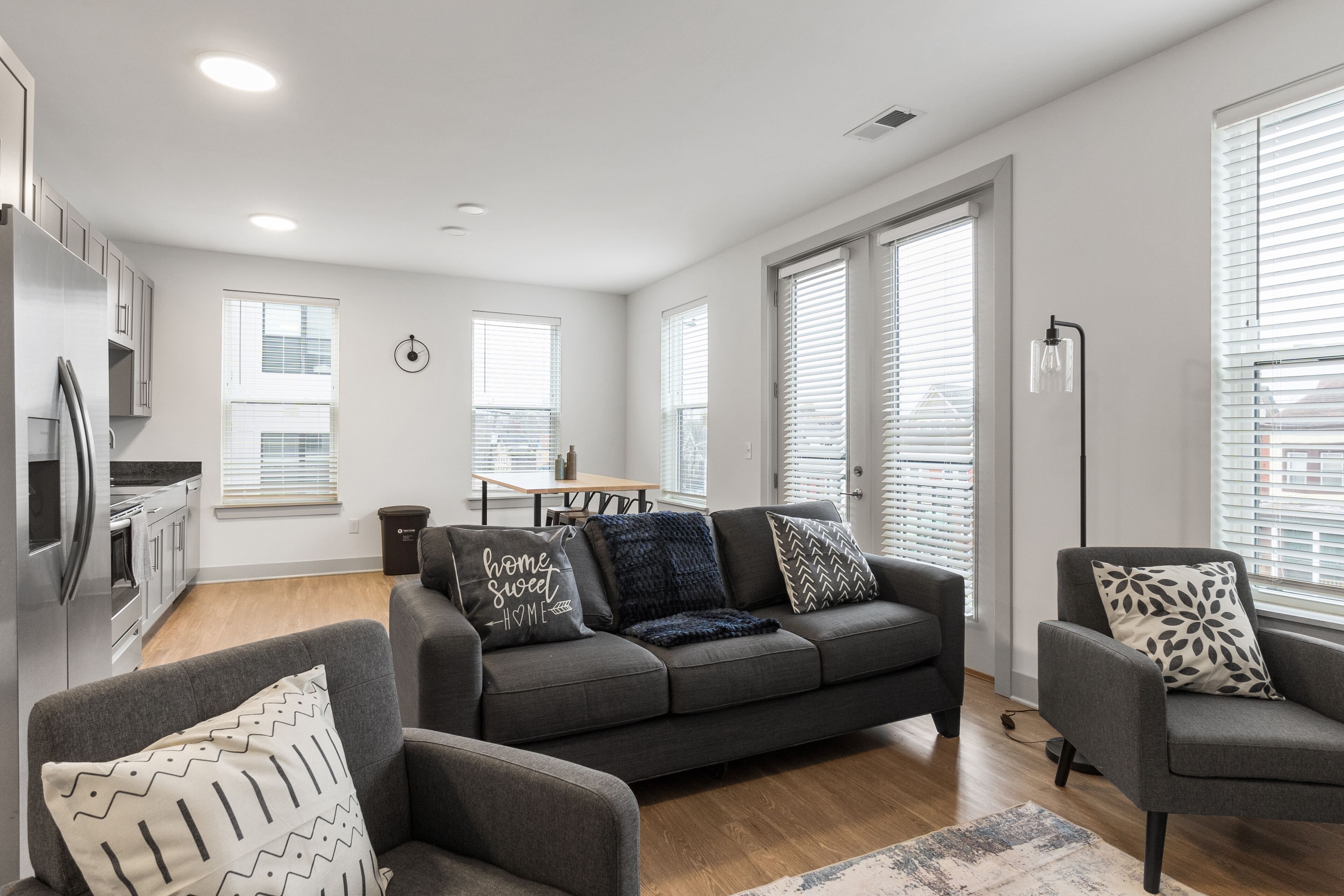 Un salon moderne avec un canapé gris, un fauteuil gris et un coin repas comprenant une table et des chaises.