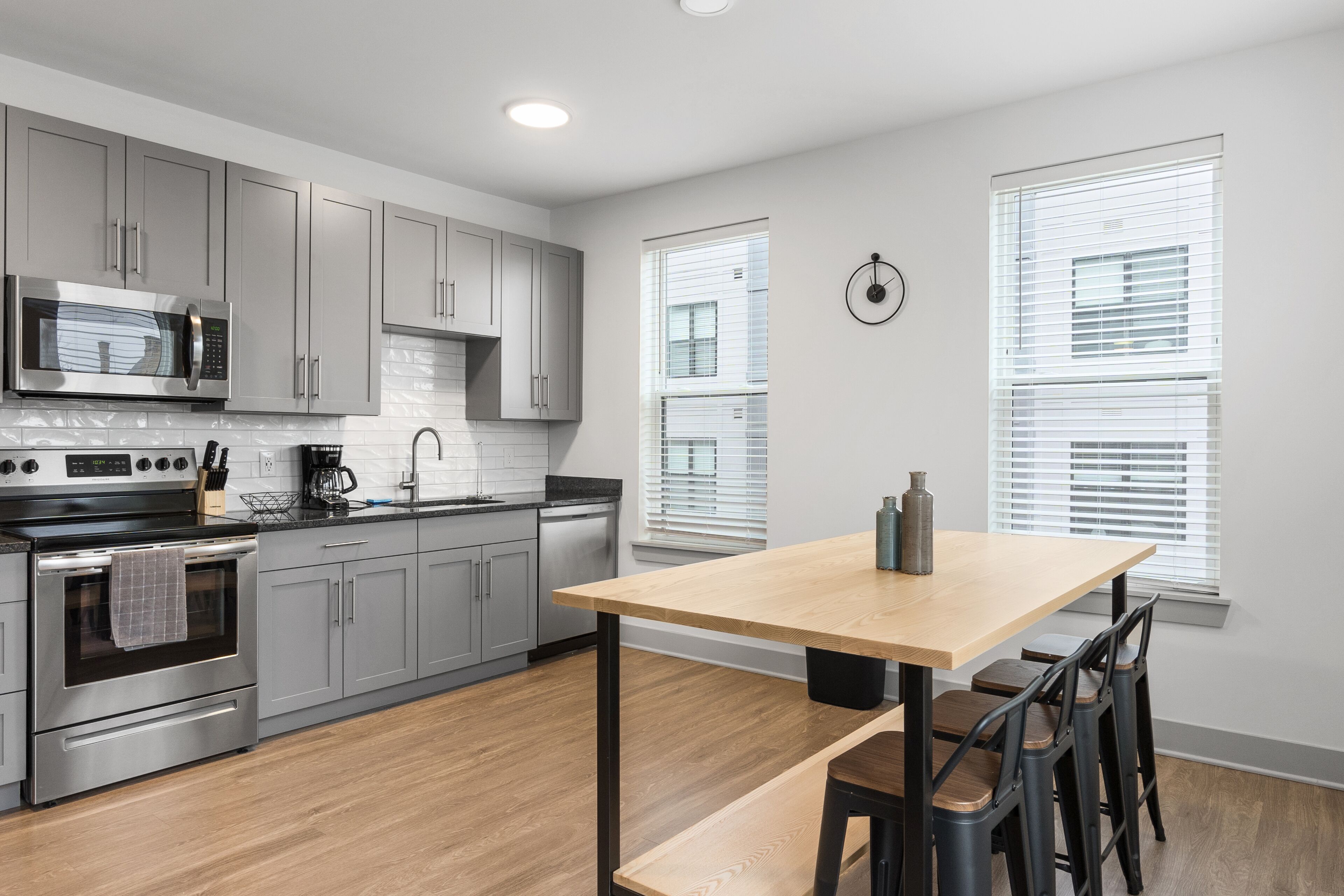 A modern kitchen with grey cabinets, a stainless steel stove, and a wooden dining table with bar stools.