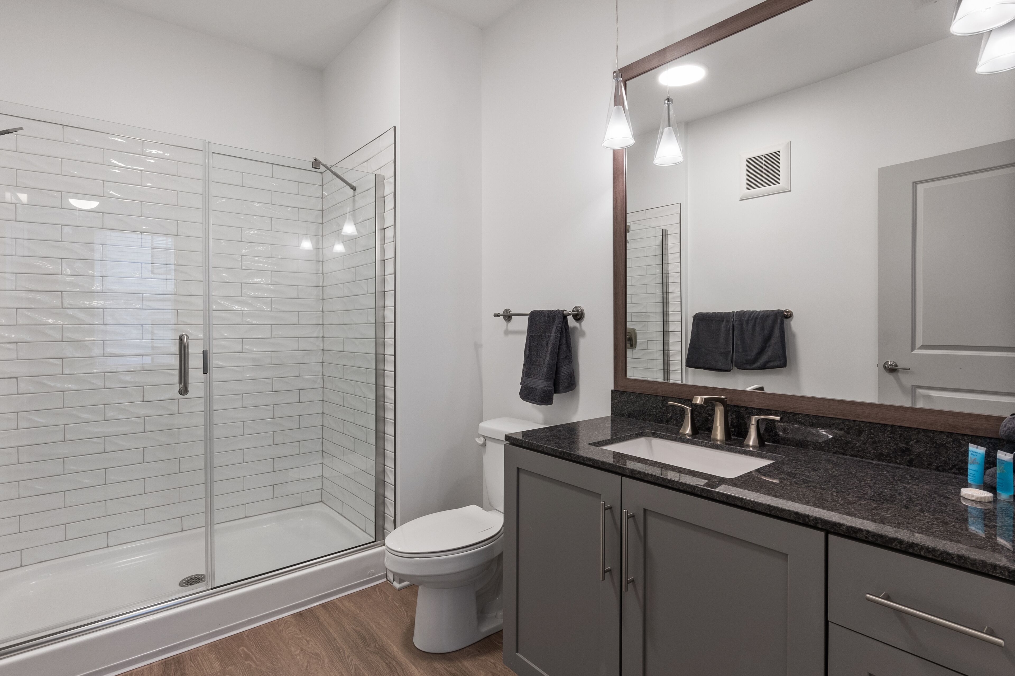 A modern bathroom with a glass shower enclosure, a white toilet, a sink with a granite countertop, and a large mirror.