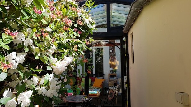 Un giardino con fiori bianchi e una serra in vetro con tavolo e sedie.