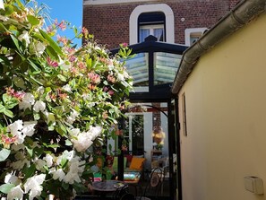 Un jardin agrémenté de fleurs blanches et une véranda en verre avec une table et des chaises.