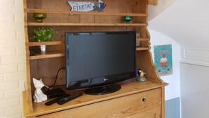 Un mobiletto TV in legno con televisore a schermo piatto, un telecomando e una piccola statuina di un gatto bianco.