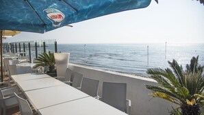 An outdoor seating area with white tables and chairs, overlooking the sea.