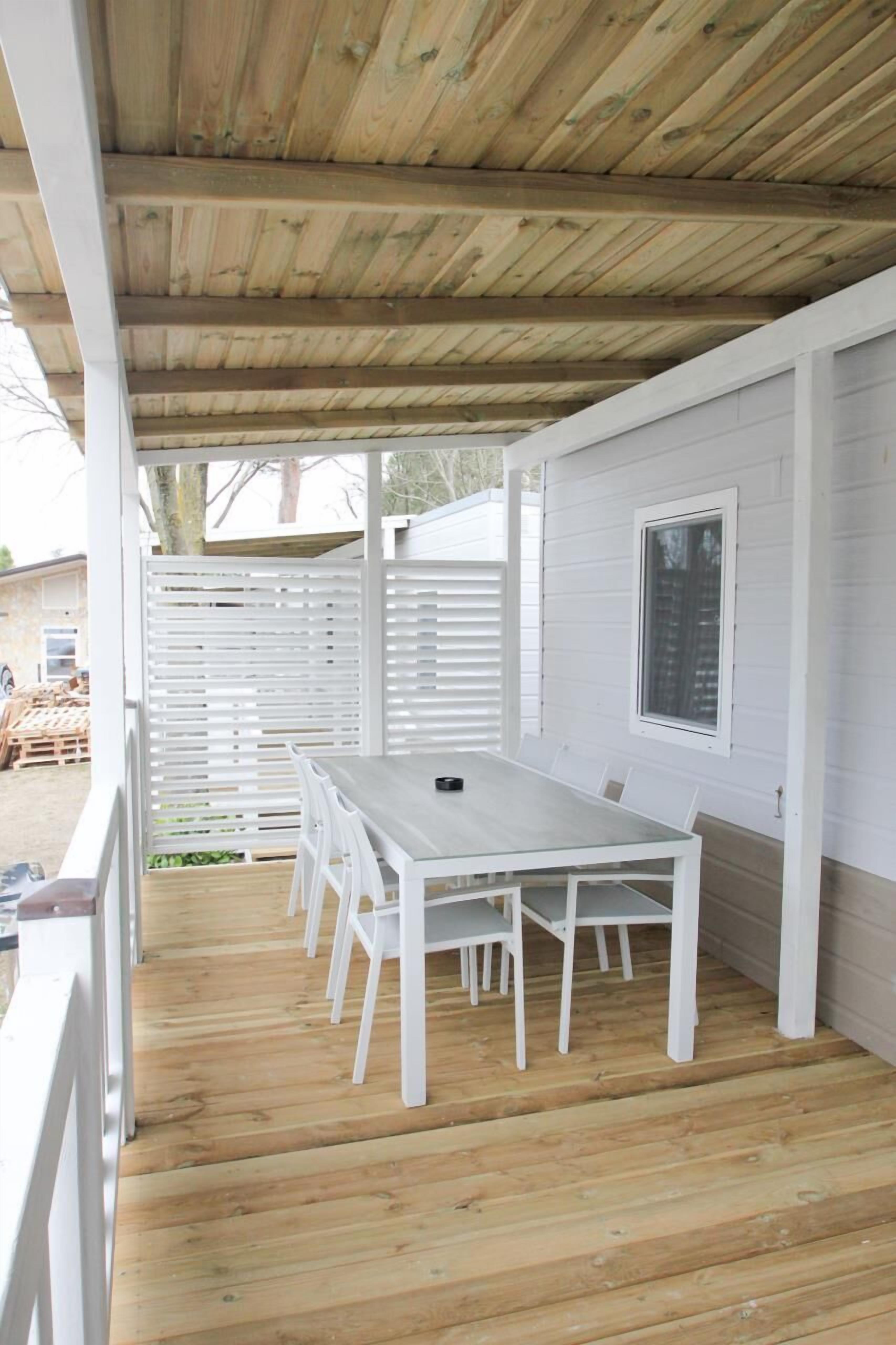 A covered outdoor patio with a wooden table and white chairs.