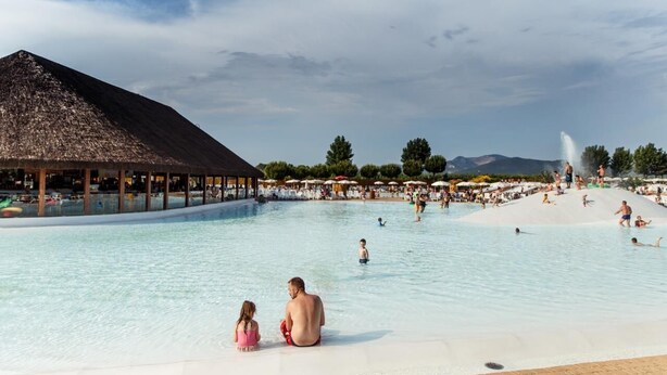 Ein großer Pool im Freien mit einem strohgedeckten Pavillon und einer Springbrunnen.