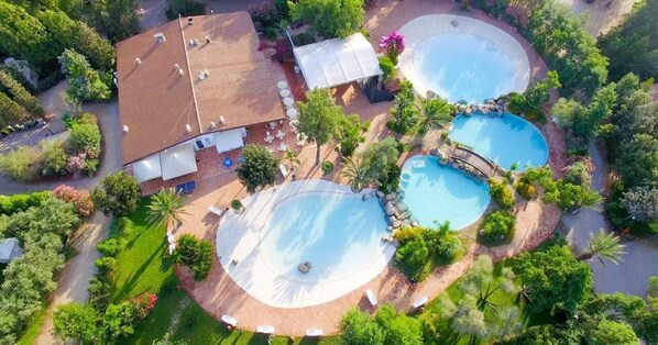 An aerial view of a resort with two large circular pools, a covered patio area, and lush landscaping.