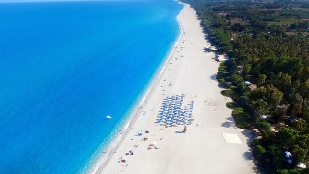An aerial view of a beach with a row of umbrellas and a few people.