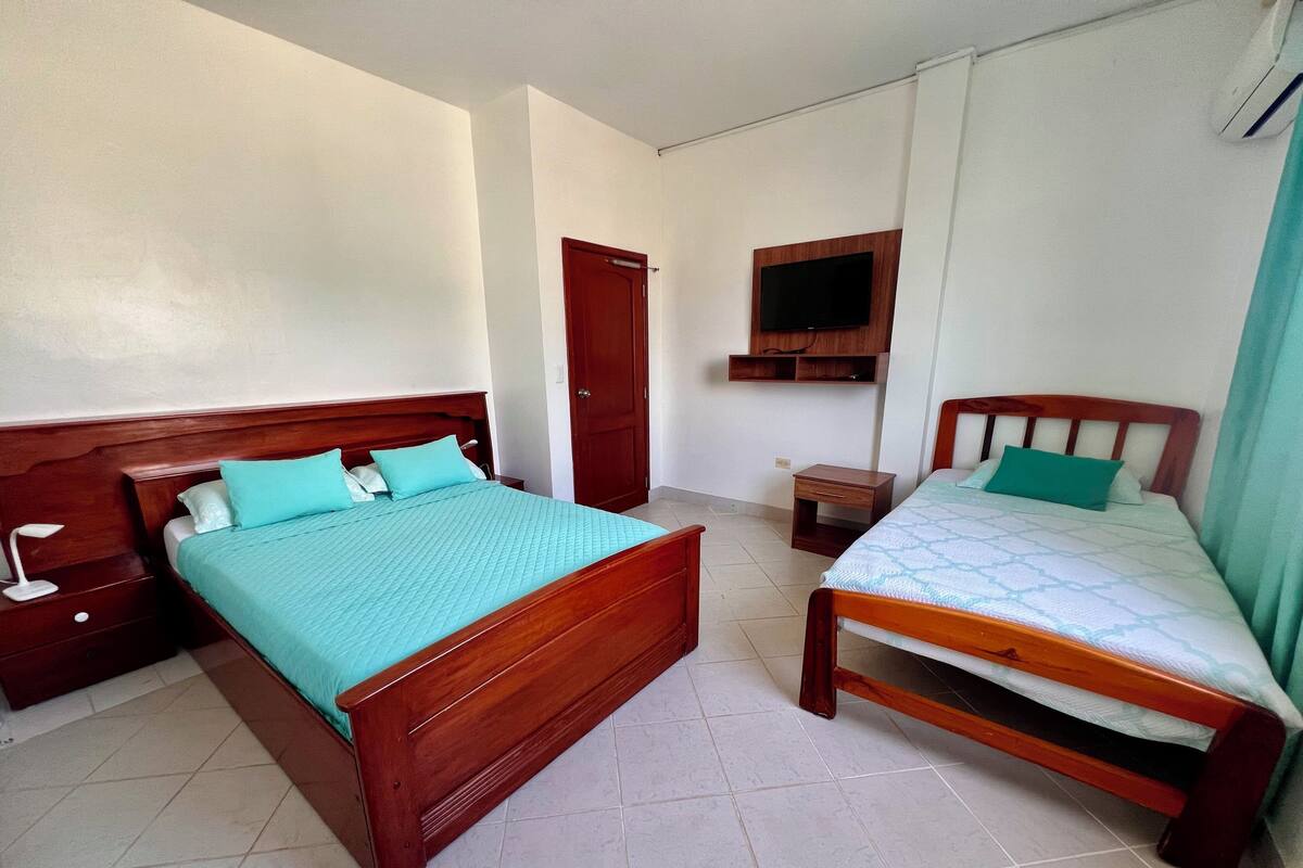 A bedroom with two wooden beds, a small wooden nightstand, a TV mounted on the wall, and a door.